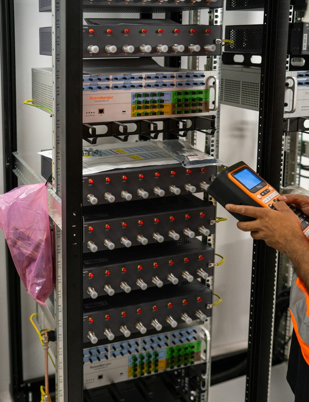 Technician testing Huawei equipment in a network rack with a handheld meter