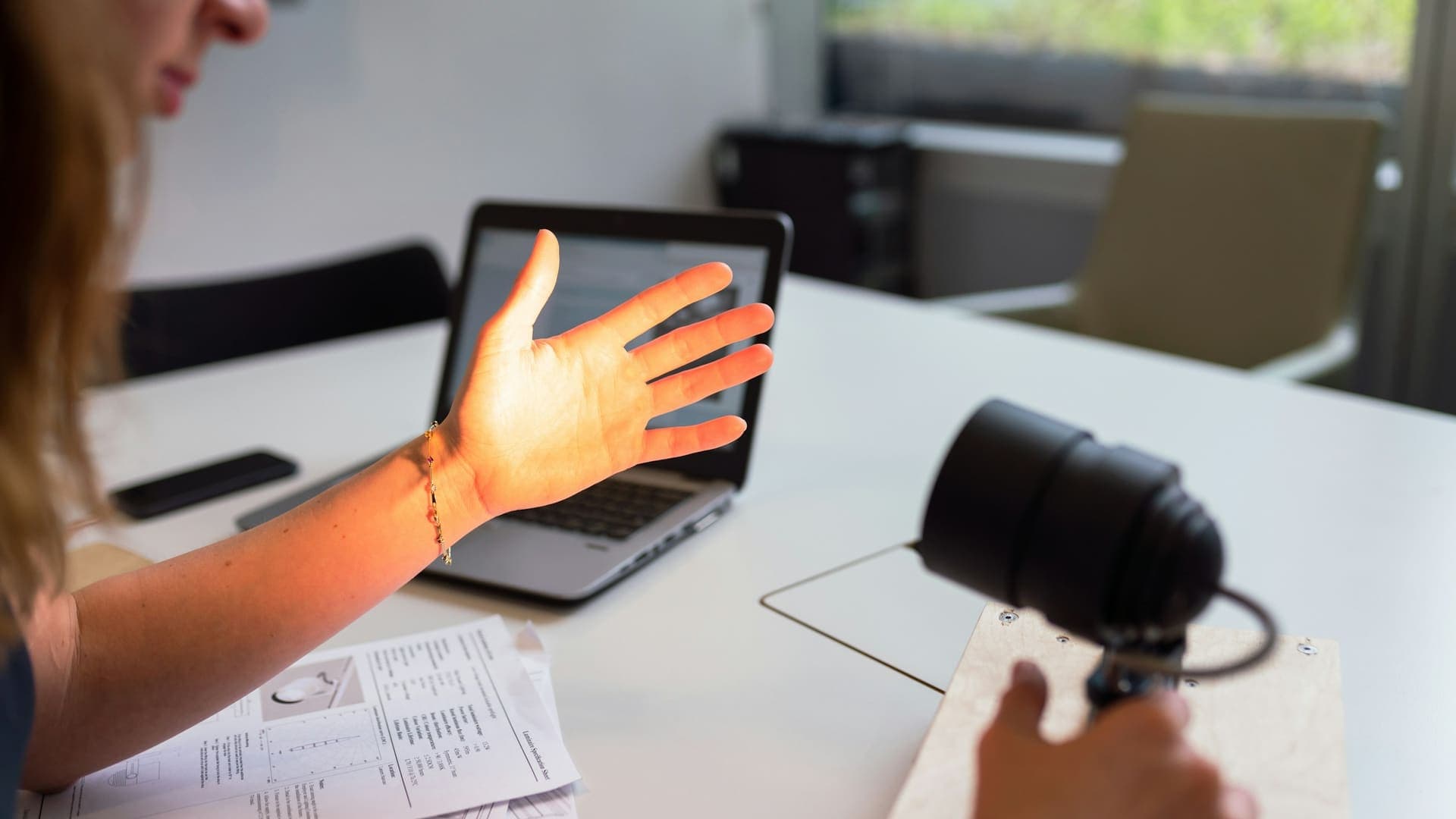 Hand gesturing at a laptop during a live online class, with a webcam on the desk