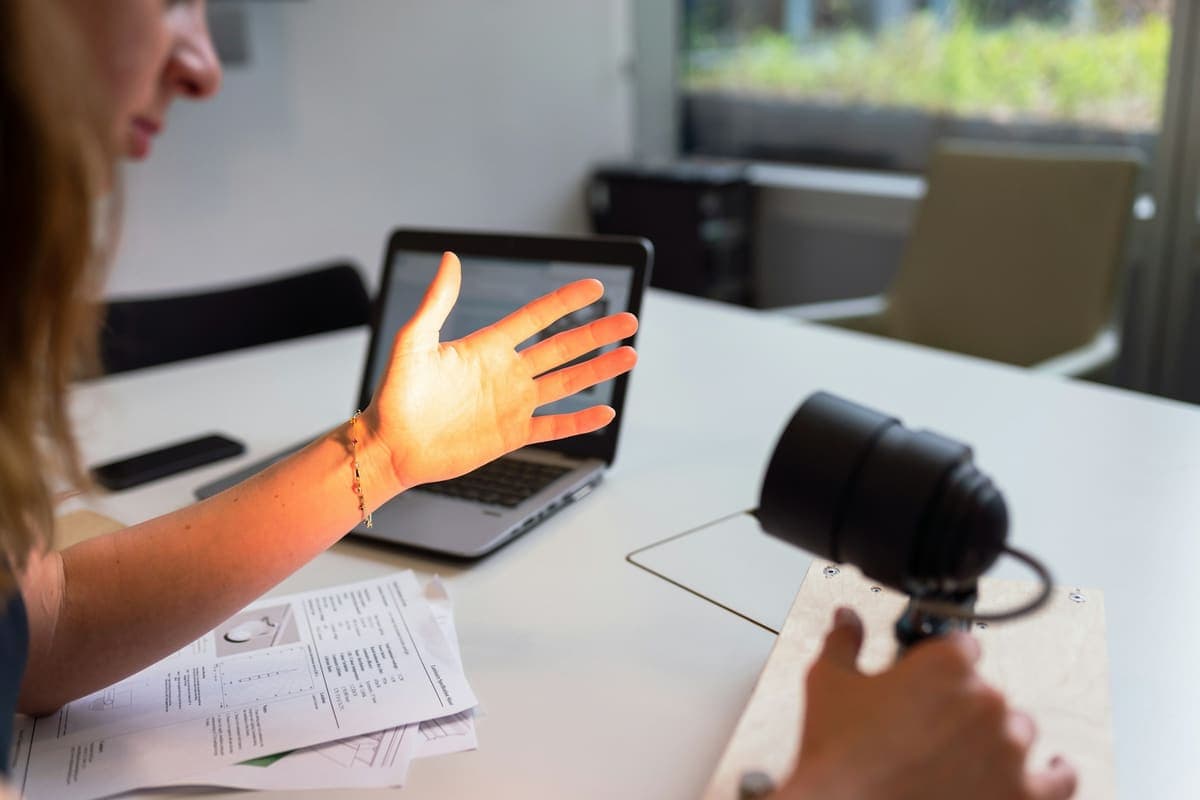 Hand gesturing at a laptop during a live online class, with a webcam on the desk