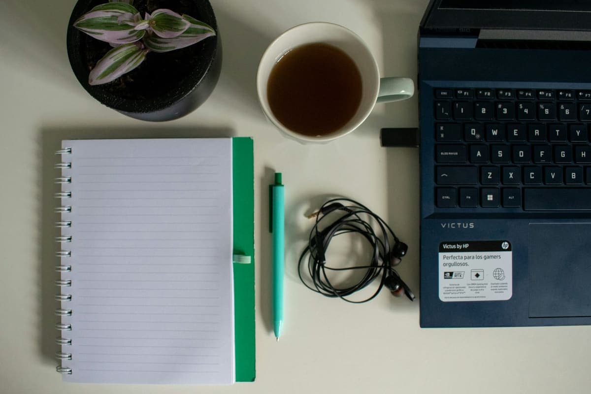 Notebook, pen, earphones and laptop laid out on a desk