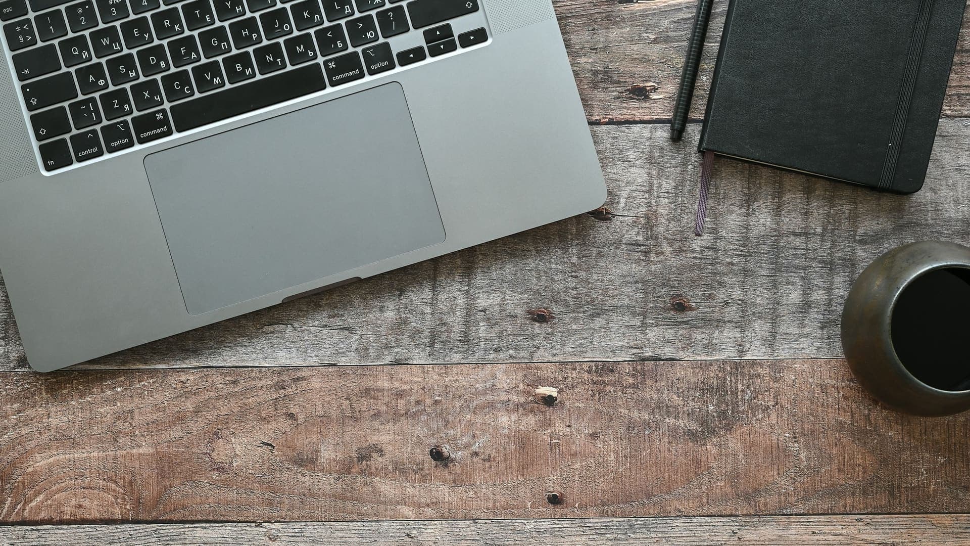 Laptop, notebook and coffee on a wooden desk, seen from above