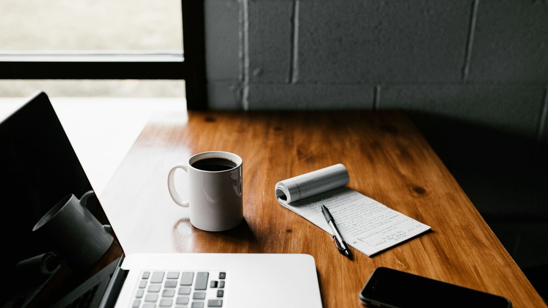 Laptop, coffee mug, notepad and phone on a wooden desk