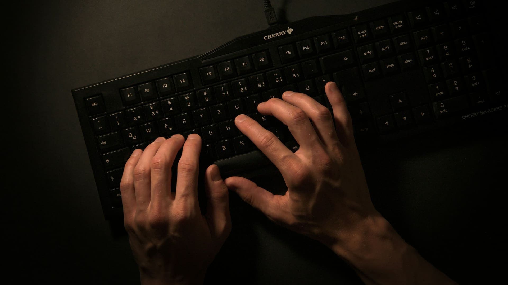 Hands typing on a keyboard in a dark room