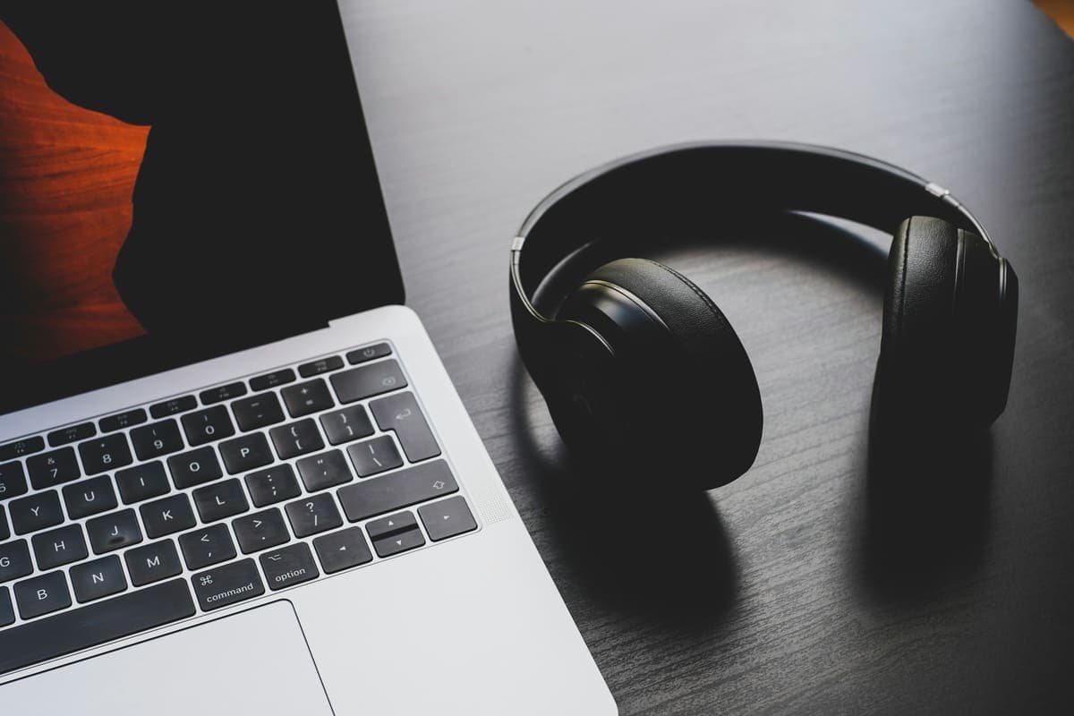 Headphones beside a laptop on a dark desk